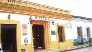 A hotel with a yellow facade, a signboard with the name 'HOTEL', and a motorcycle parked outside.