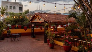 Un patio al aire libre con techo de tejas rojas, plantas en macetas y luces colgantes.