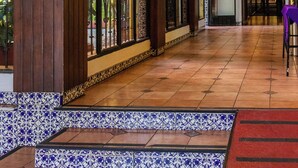Un pasillo de hotel con columnas de madera, suelo de baldosas y una araña.
