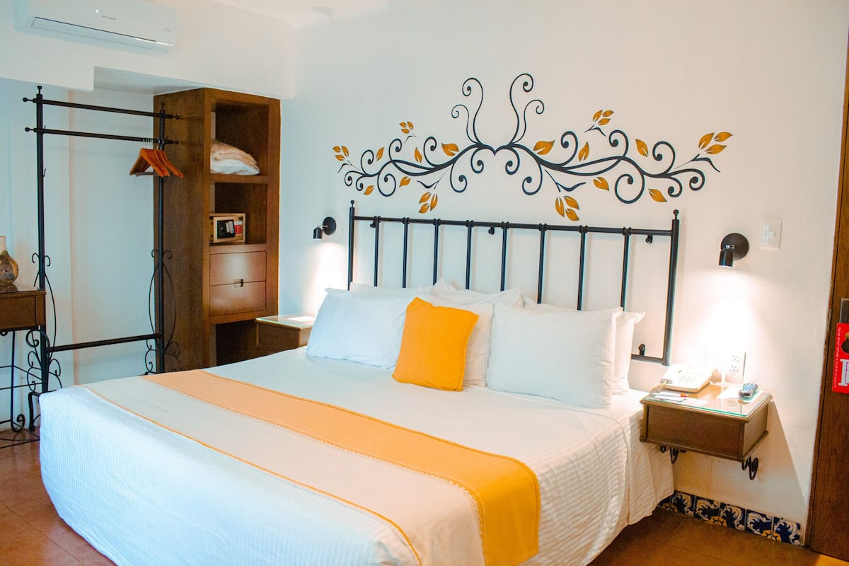 A neatly made bed with a white and orange bedspread, a wooden nightstand with a lamp, and a decorative wall design.