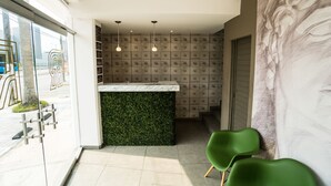 Una zona de recepción con una pared verde, una barra de mármol y un ventanal amplio.
