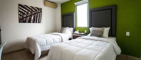 Una habitación con dos camas, una pared verde decorativa, una ventana y un cuadro.