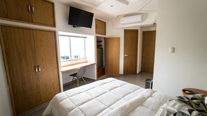 Un dormitorio con una cama grande, un armario de madera, un escritorio con silla, un televisor y un equipo de aire acondicionado.
