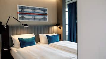 Una camera d'albergo con un letto, un comodino, una lampada, un'opera d'arte appesa al muro e una finestra con tende.