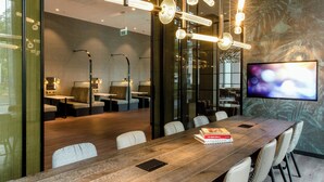 A modern conference room with a long wooden table, comfortable seating, and a large screen on the wall.