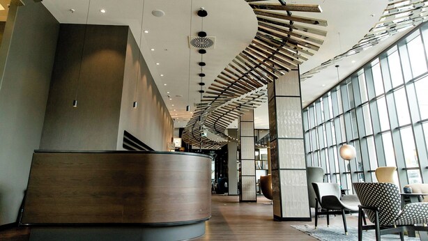 A modern interior with a curved reception desk, a high ceiling with unique lighting fixtures, and large windows providing natural light.
