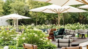 An outdoor seating area with multiple chairs and tables, surrounded by lush greenery and white flowers.
