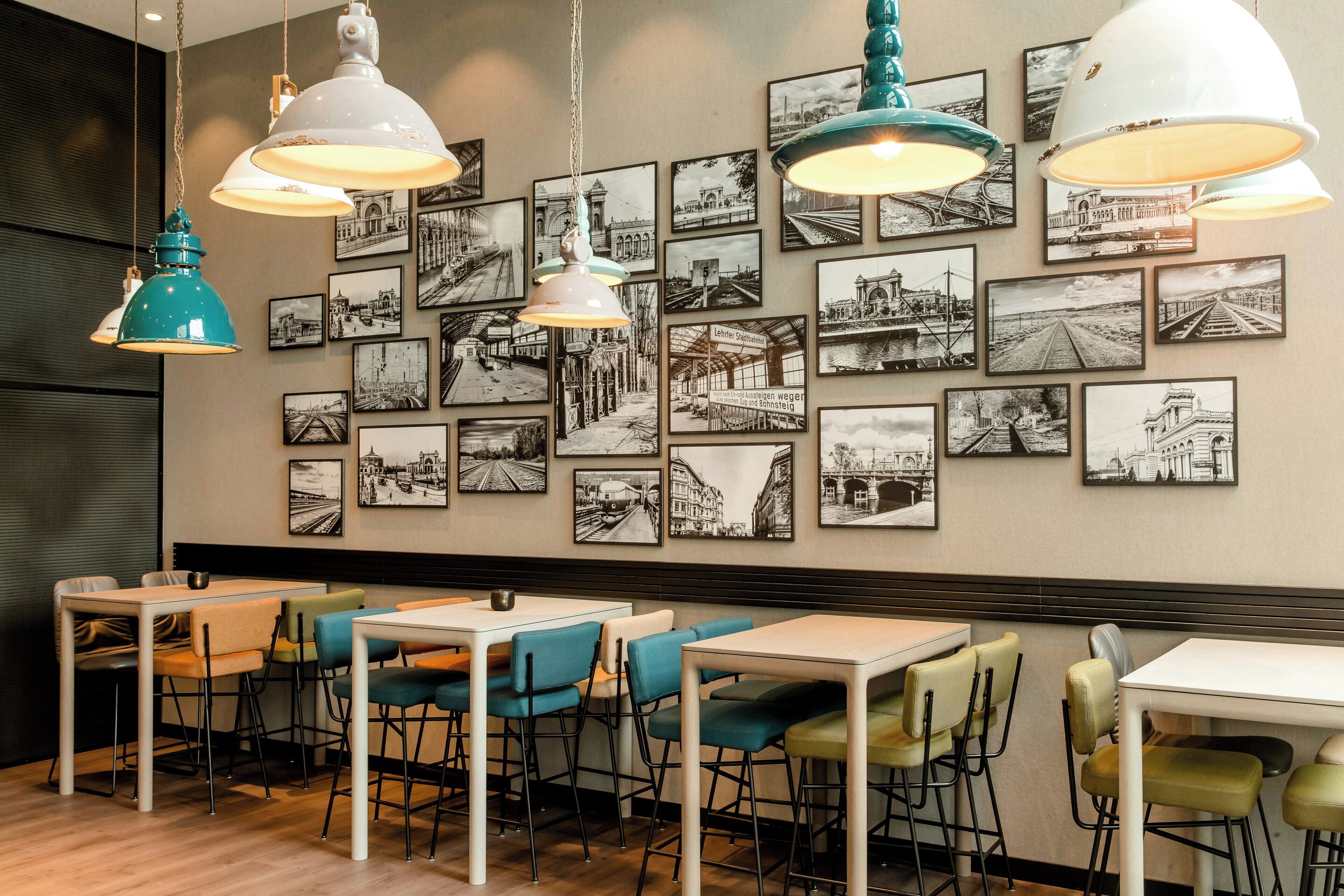 A restaurant interior with multiple tables and chairs, black and white photographs on the wall, and pendant lighting.