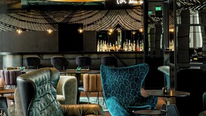 A modern bar area with leather chairs, a patterned armchair, and a large hanging light fixture.