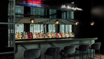 A bar area with a variety of liquor bottles, hanging pendant lights, and bar stools.