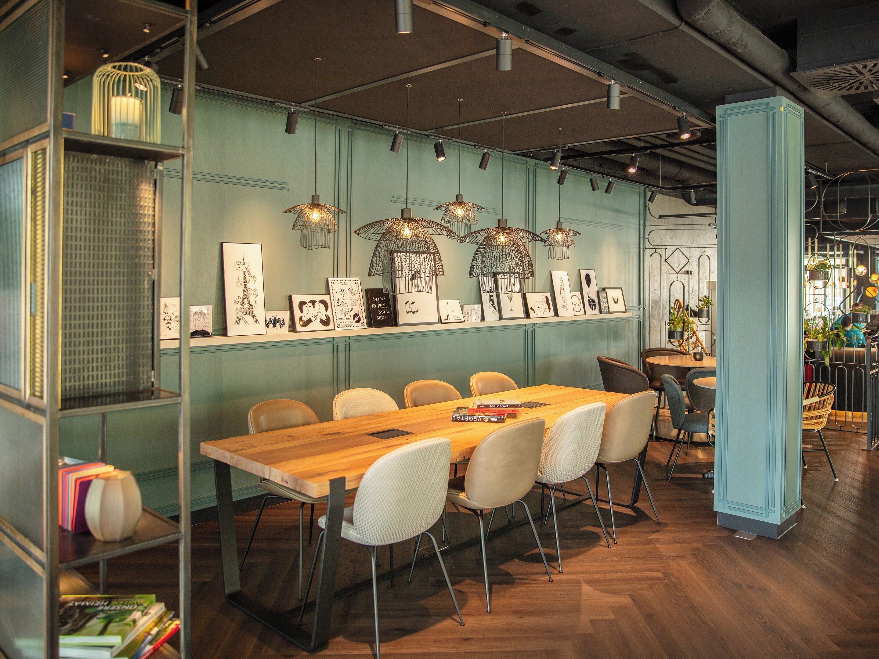 A modern dining area with a long wooden table, white chairs, and pendant lights.