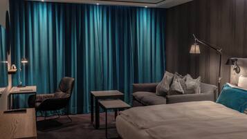Habitación de hotel con una cama grande, un sofá, un escritorio y una silla. Hay dos lámparas y una cortina.