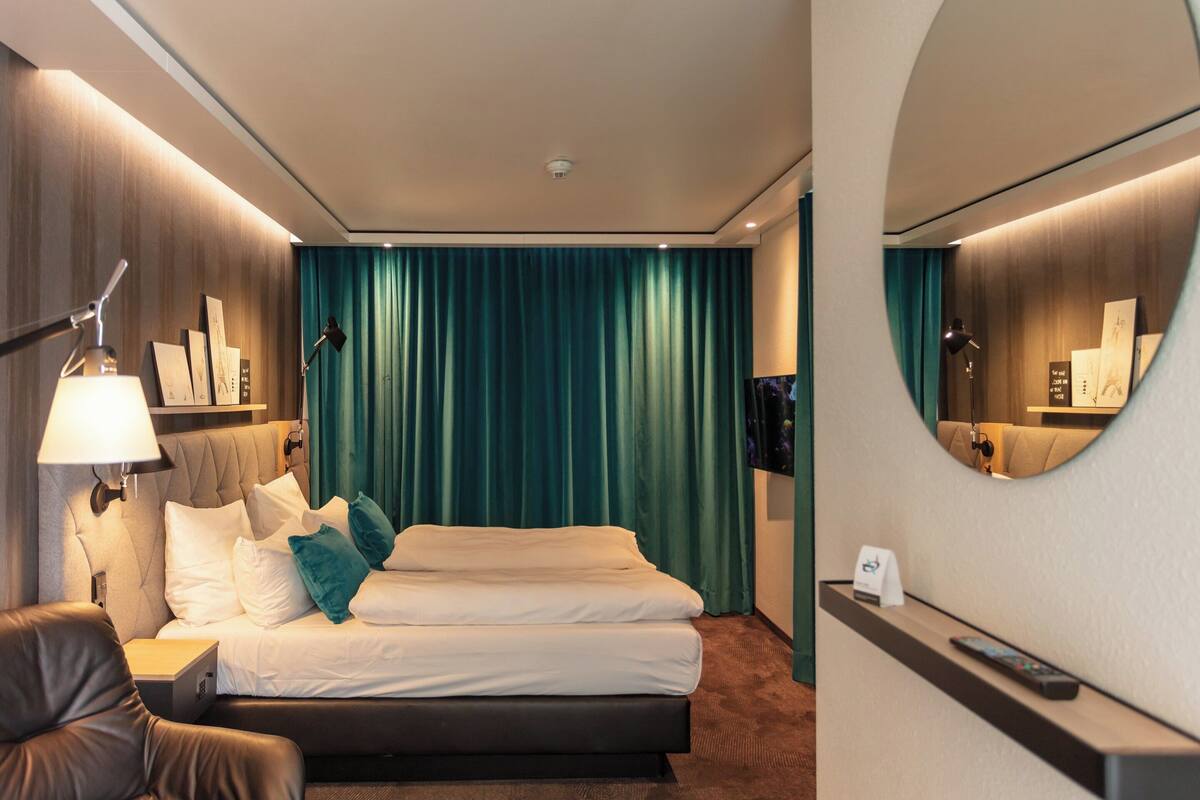 Una habitación de hotel con cama, escritorio, silla, televisor y espejo.