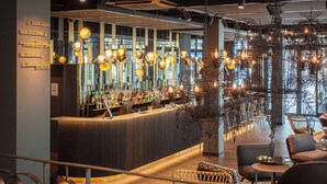 A modern bar area with a long counter, hanging light fixtures, and wicker furniture. - Motel One Saarbrücken (Saarbrücken)