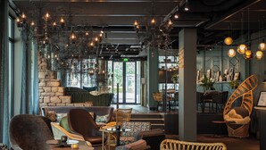 A modern lounge area with comfortable seating, a stone wall, and a bar area with hanging lights. - Motel One Saarbrücken (Saarbrücken)
