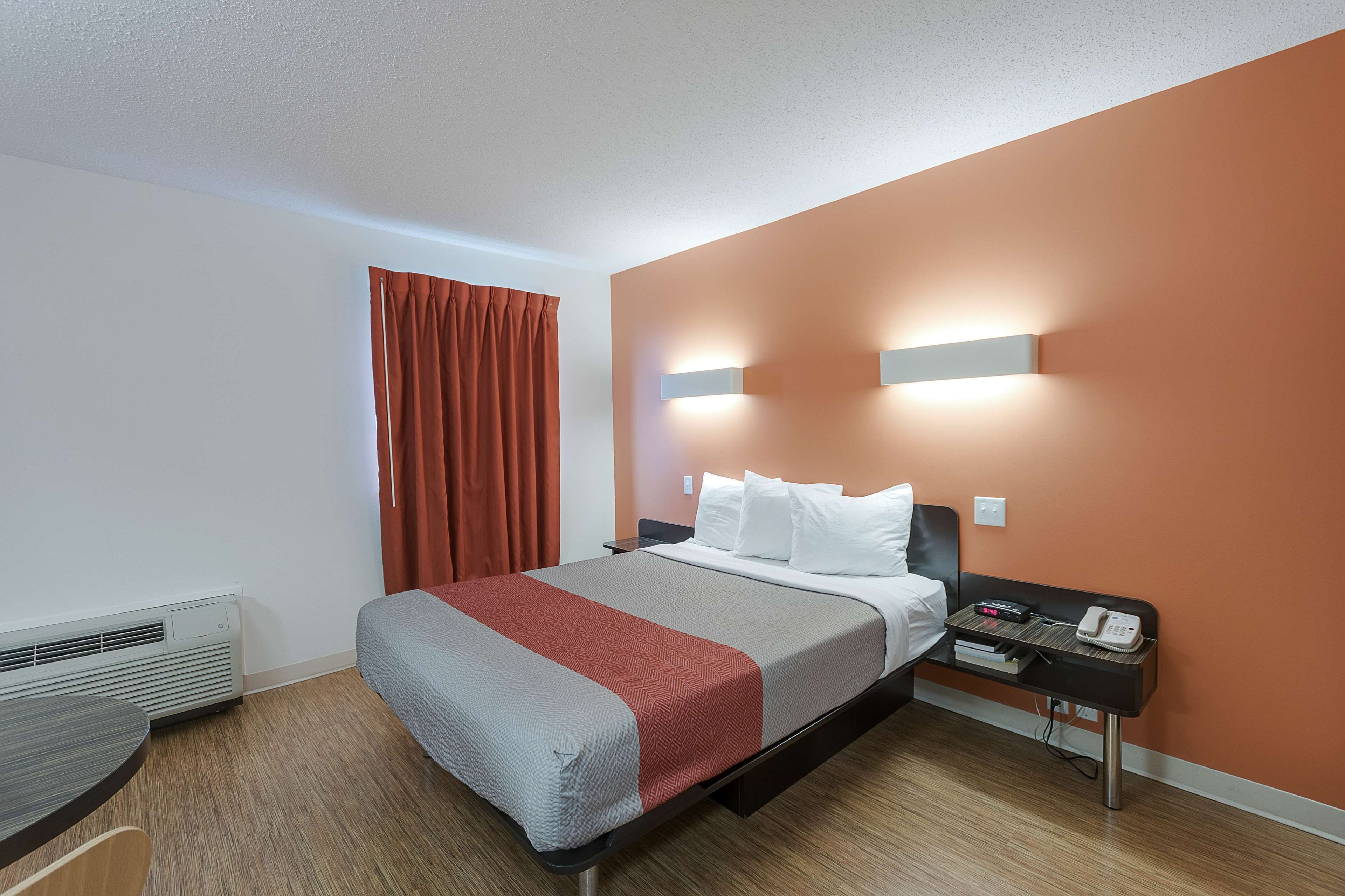A hotel room with a bed, a nightstand, a phone, and a heater.