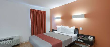 A hotel room with a bed, a nightstand, a phone, and a heater.