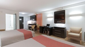 A hotel room with two beds, a desk, a chair, a TV, and a kitchenette. - Motel 6 Brandon, MB (Brandon)