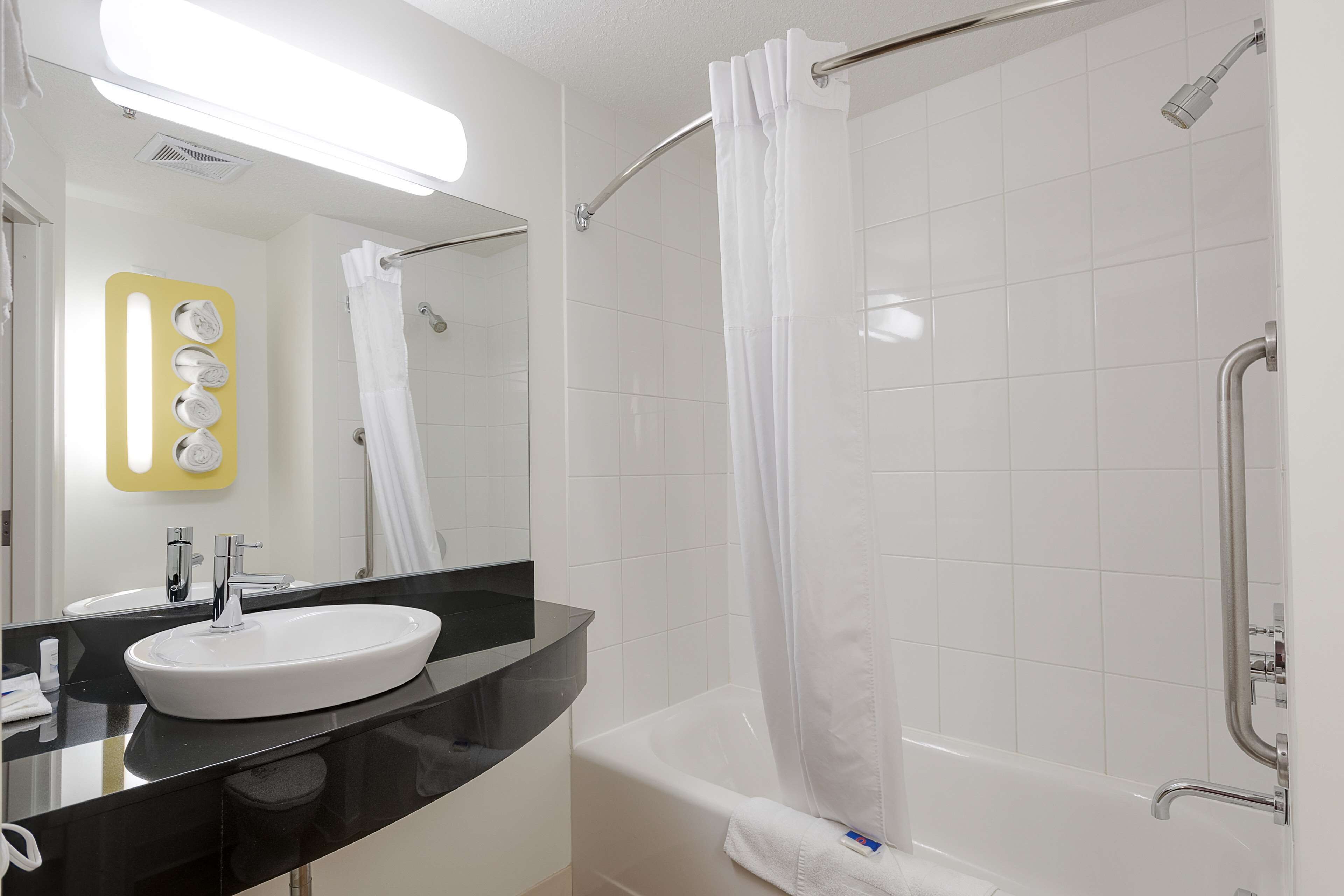A modern bathroom with a white sink, black countertop, and a bathtub with a shower curtain.