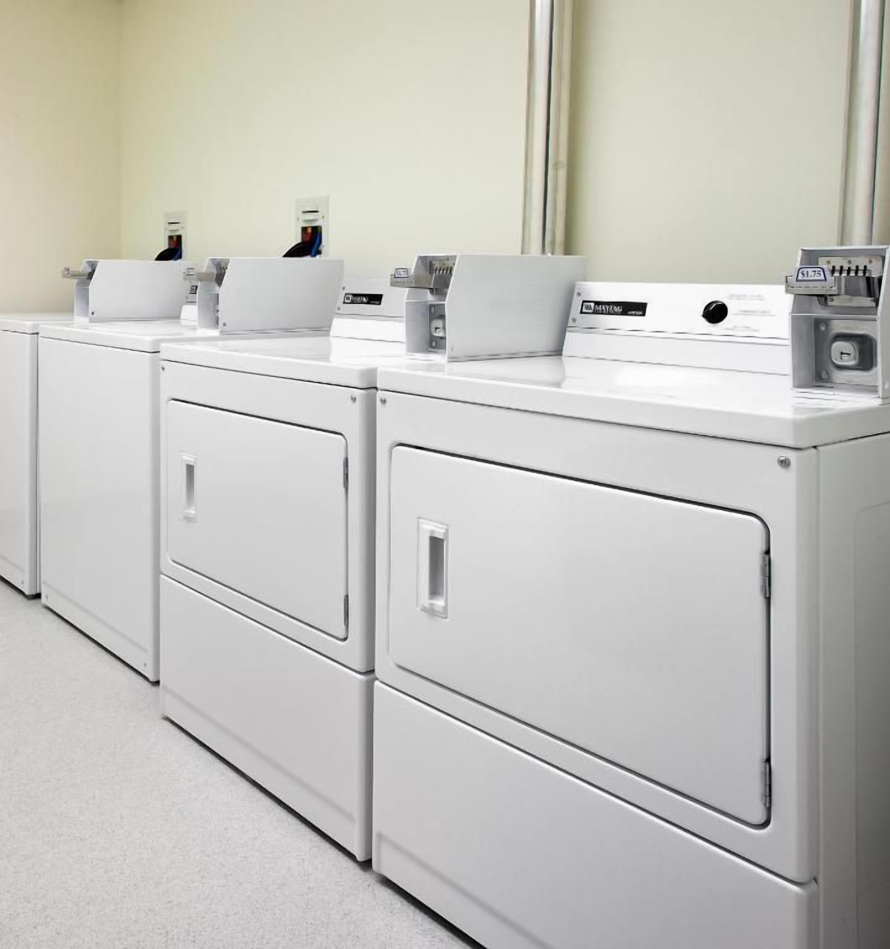 Een rij witte wasmachines in een ruimte met een effen muur en een spiegel.