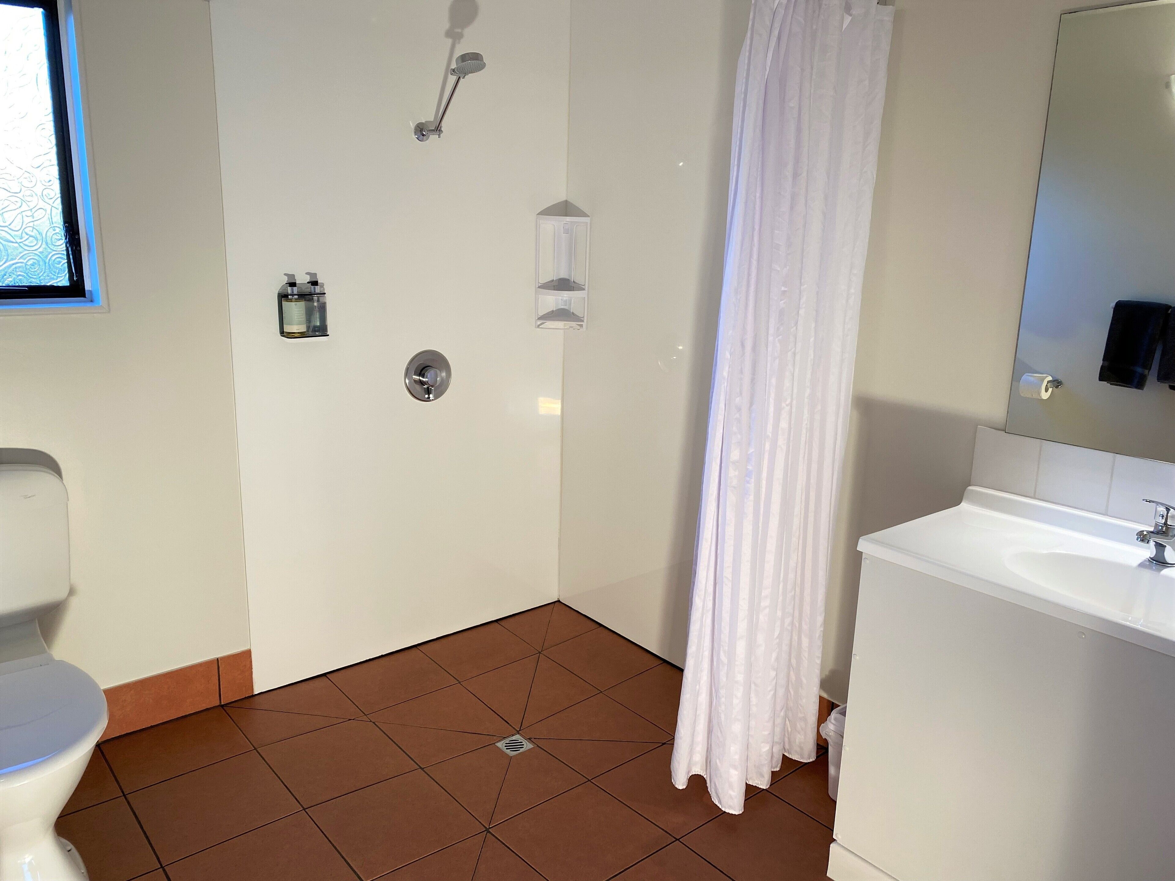 A bathroom with a toilet, sink, shower, and a mirror.