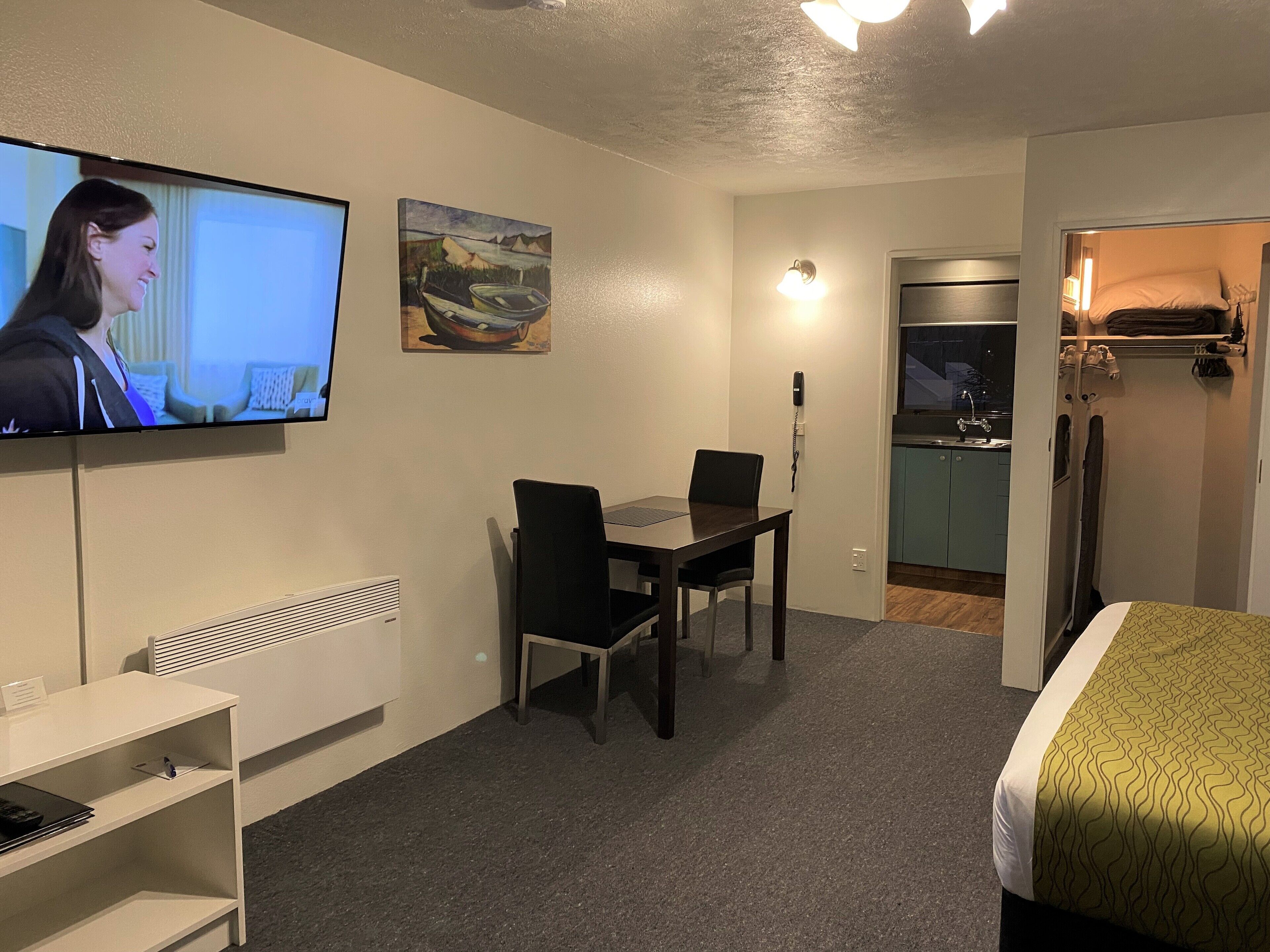 Habitación de hotel con cama, televisión, mesa de comedor con sillas, zona de cocina y baño.