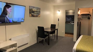 Habitación de hotel con cama, televisión, mesa de comedor con sillas, zona de cocina y baño.
