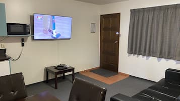 Ein Wohnzimmer mit Fernseher, einer Tür, einem kleinen Tisch und einer Couch.