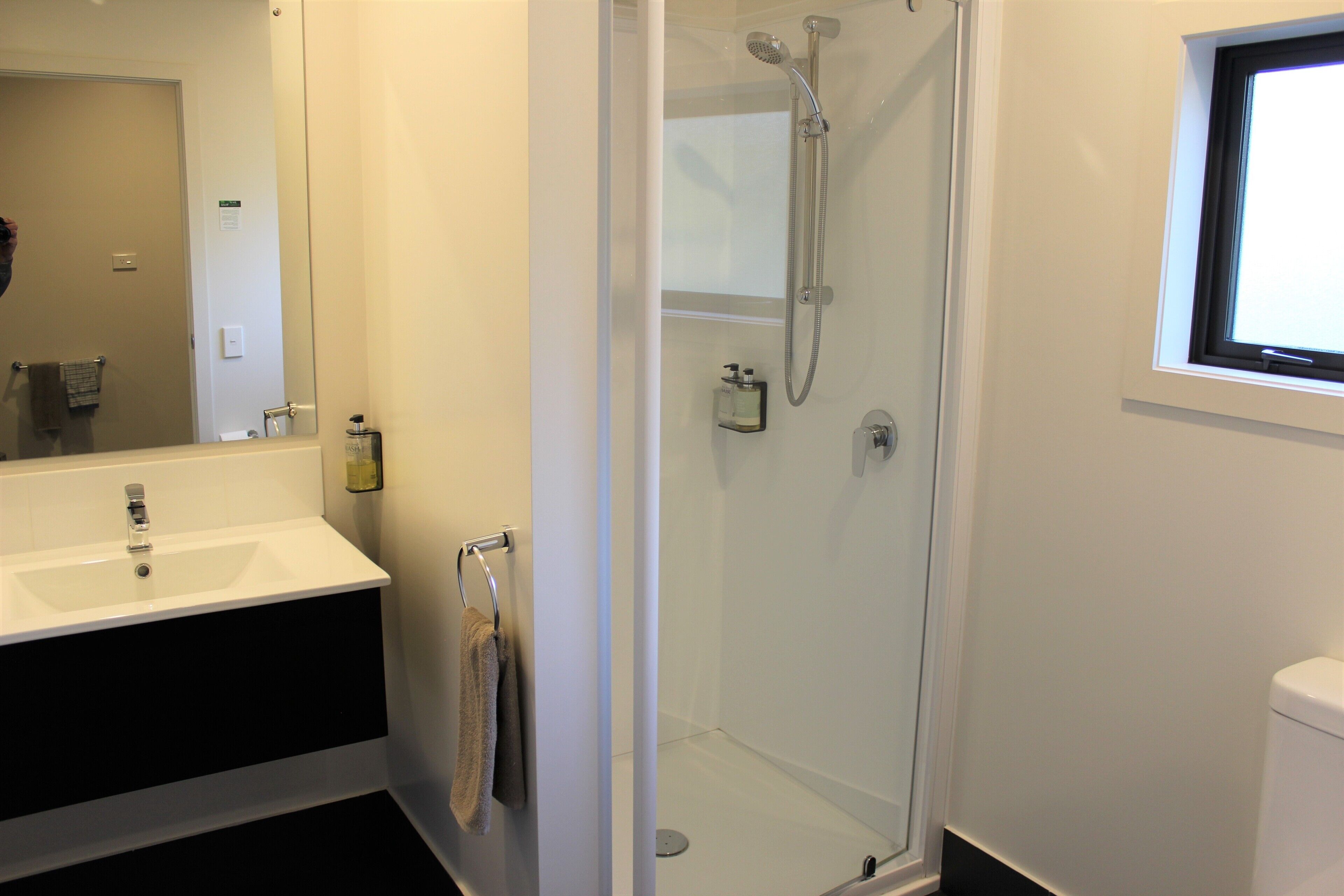 A bathroom with a glass-enclosed shower, a white sink, and a window above the toilet.