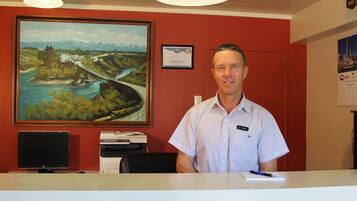 A man in a striped shirt at a reception desk with a painting of a bridge and mountains on the wall.