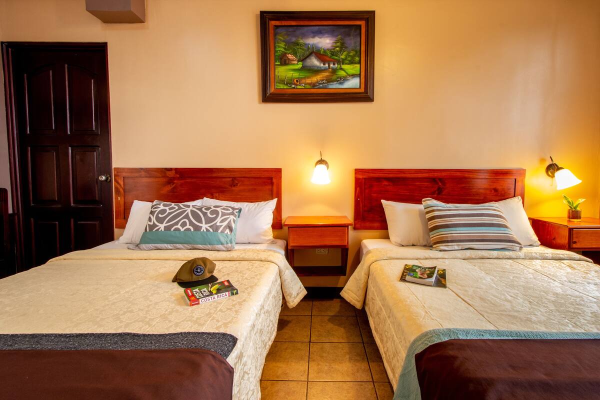 Habitación de hotel con dos camas, cabeceros de madera, un cuadro en la pared y una puerta.