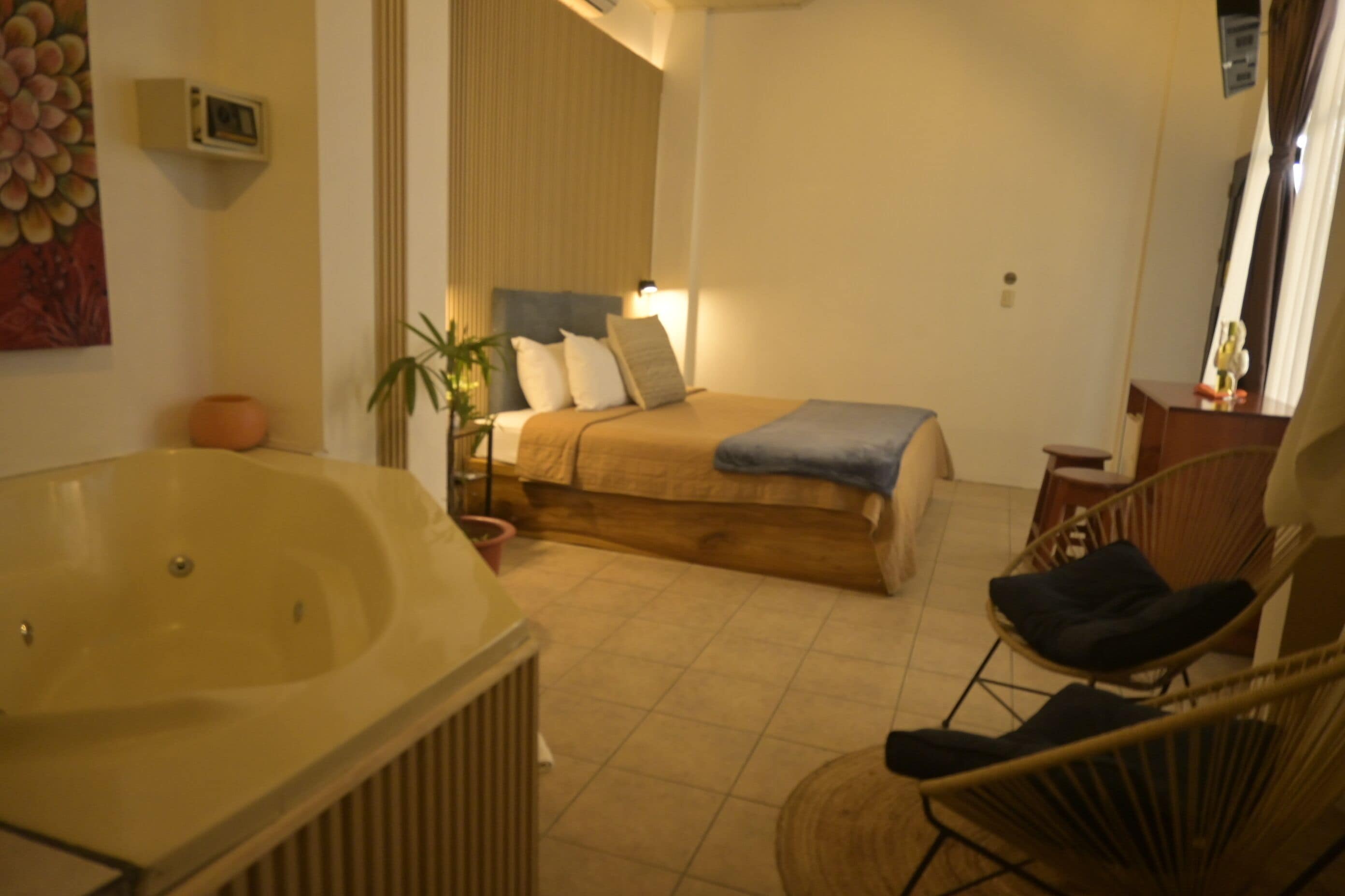 Een slaapkamer met een groot bad, een bed met een blauwe deken, een stoel en een kamerplant.