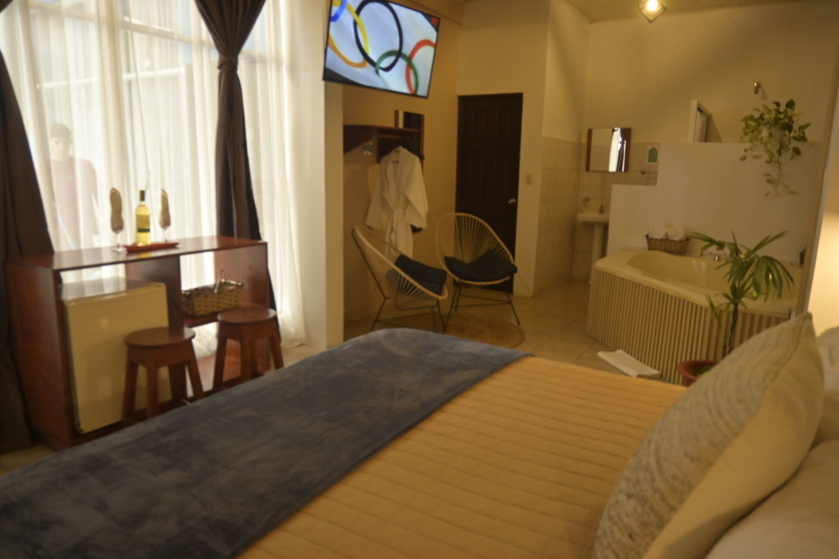 A hotel room with a bed, a desk, a chair, a bathtub, and a TV displaying the Olympic rings.