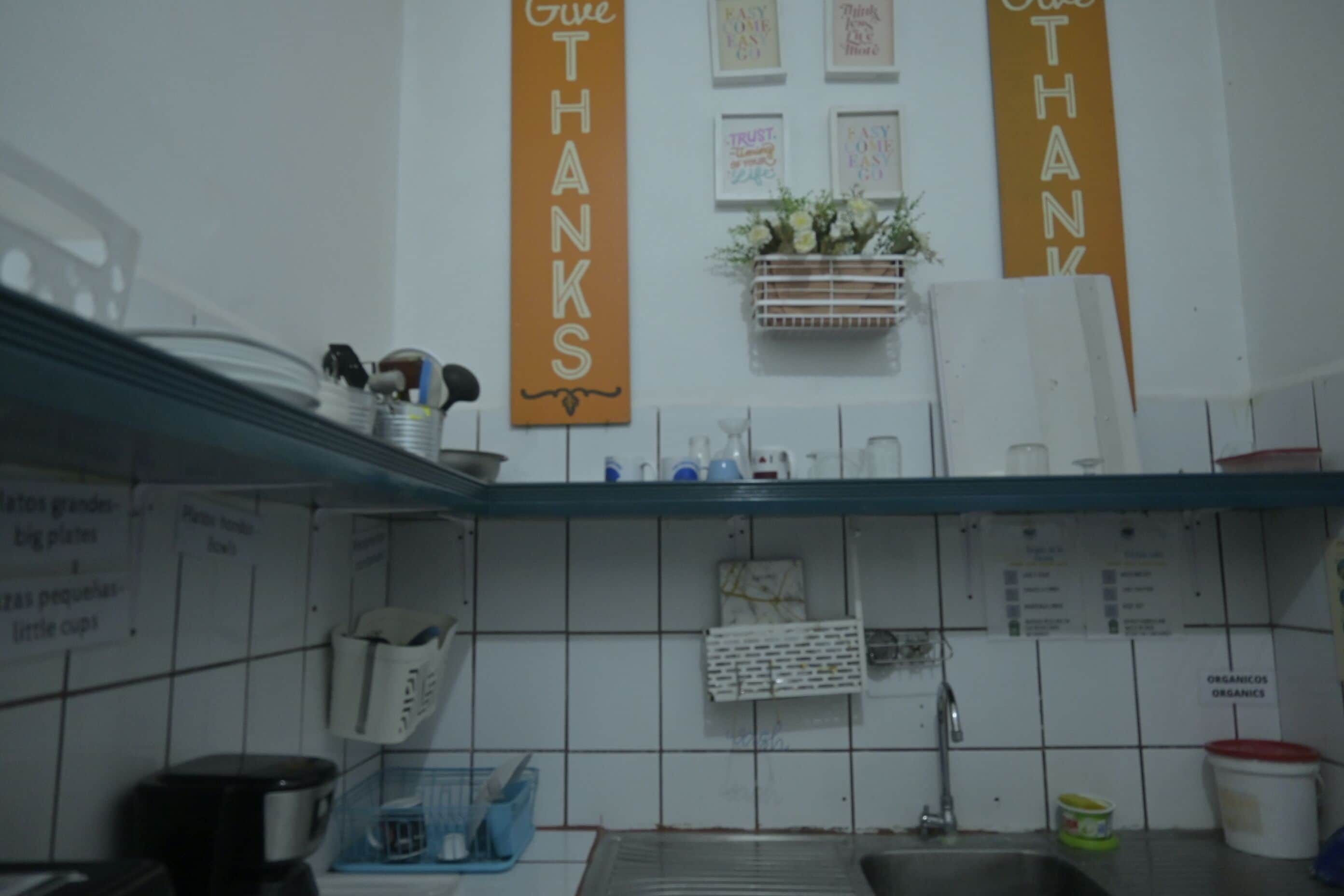 A kitchen with white tiles, a sink, and a countertop with various items. There are two orange banners with the word "THANKS" on them.
