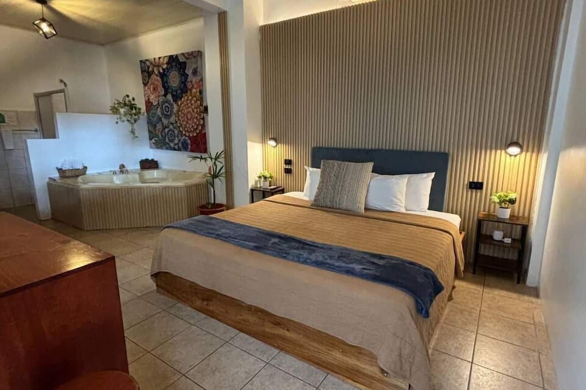 Un dormitorio moderno con una cama grande, un escritorio de madera y un baño visible al fondo.