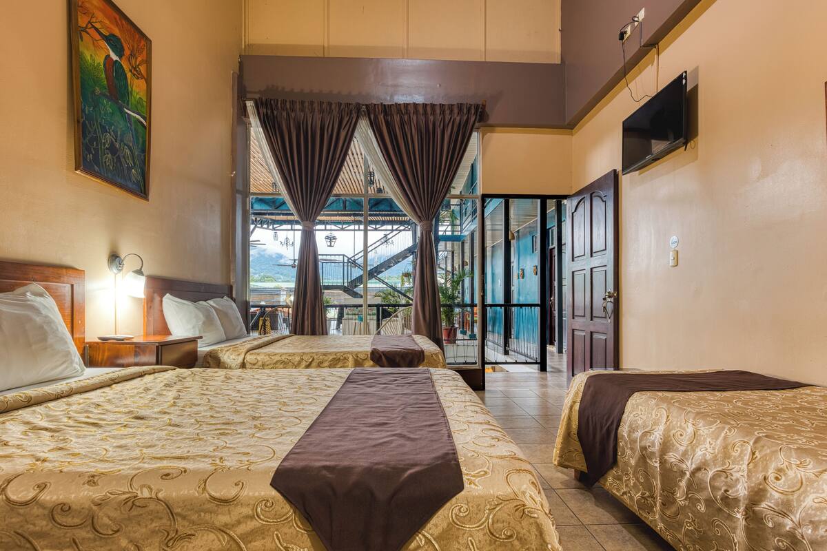 Habitación de hotel con dos camas, un televisor y vista a una escalera que lleva a un balcón.