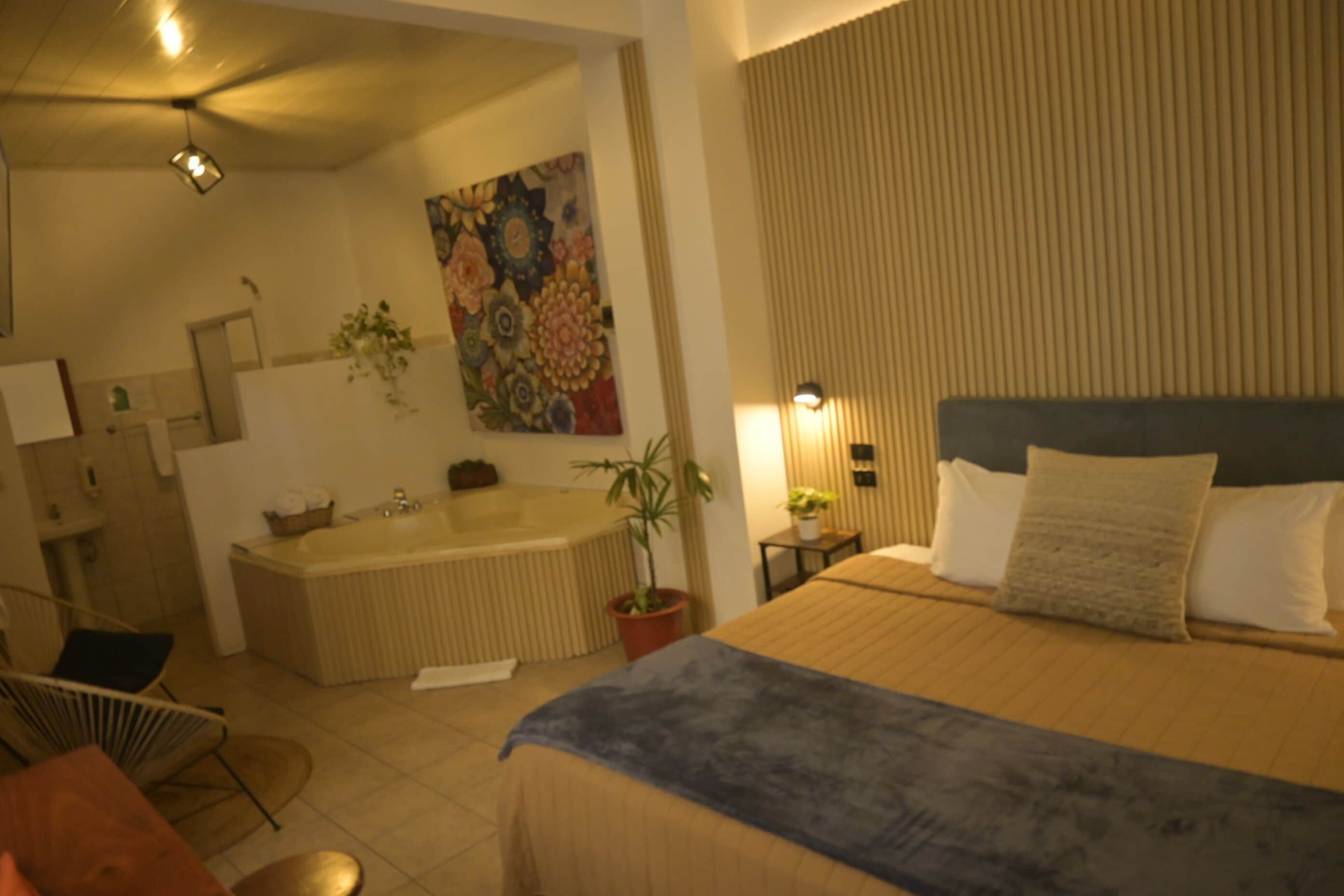 A bedroom with a large bed, a bedside table, a nightstand, a wall-mounted TV, and a bathroom with a bathtub and sink.