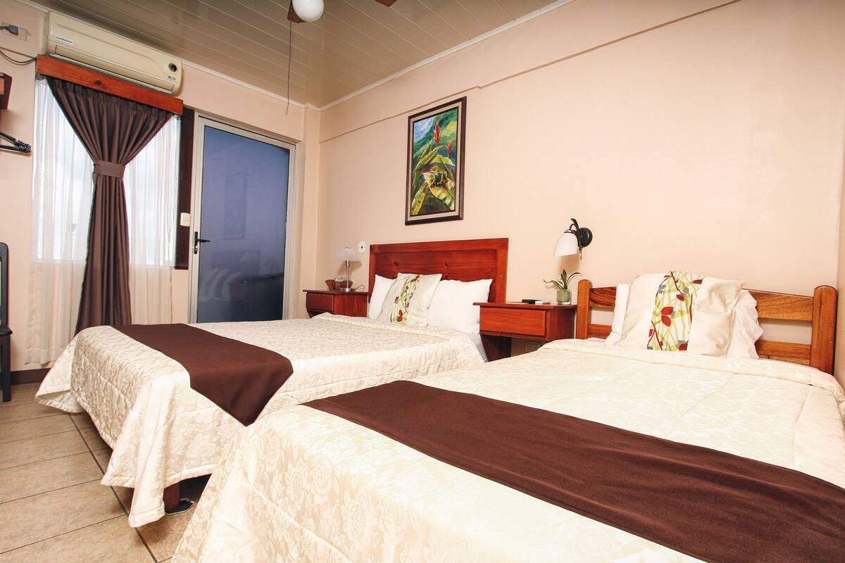 Habitación de hotel con dos camas, un cuadro en la pared y un ventilador de techo.