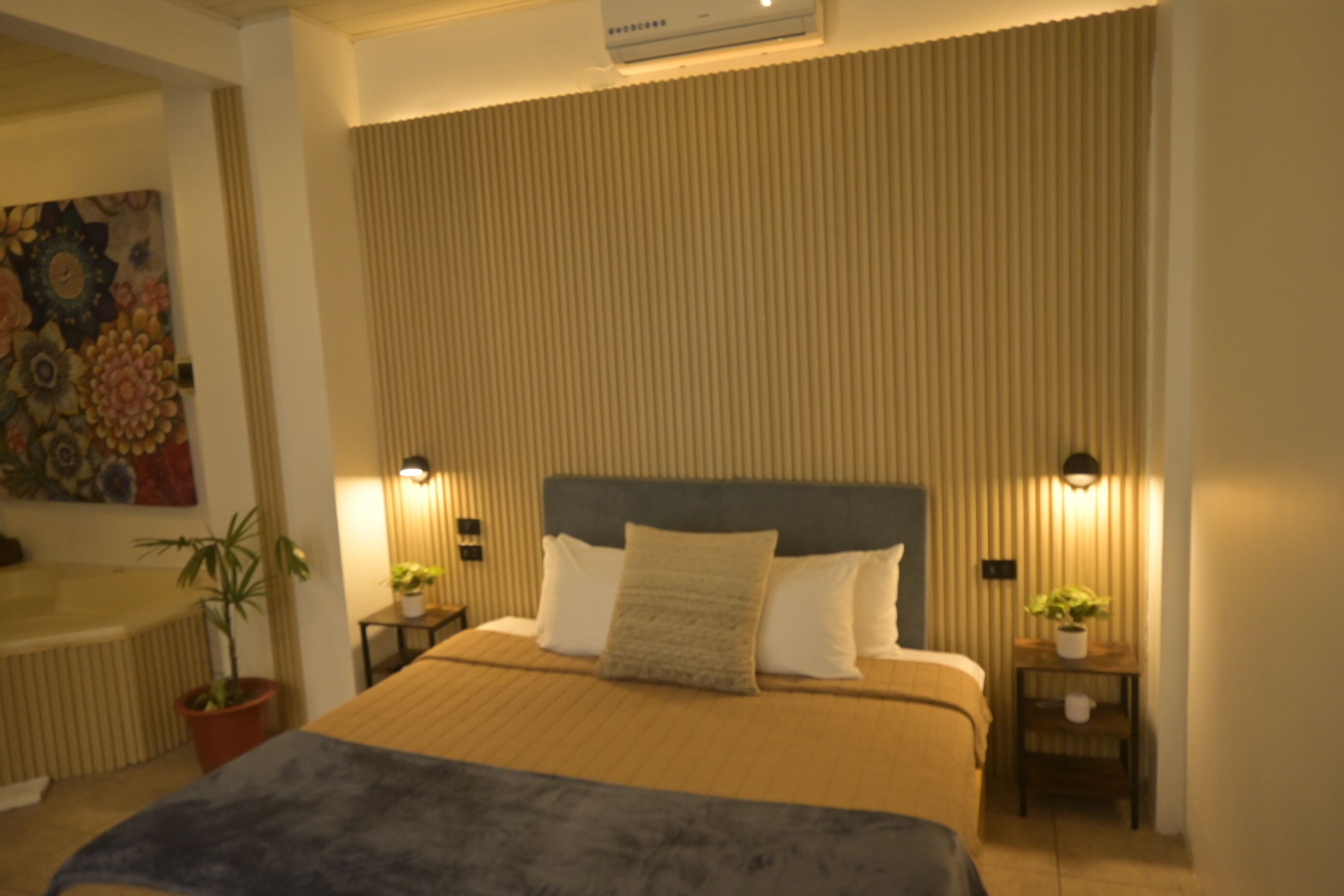 A neatly arranged bedroom with a large bed, two bedside tables with lamps, and a potted plant on each side.