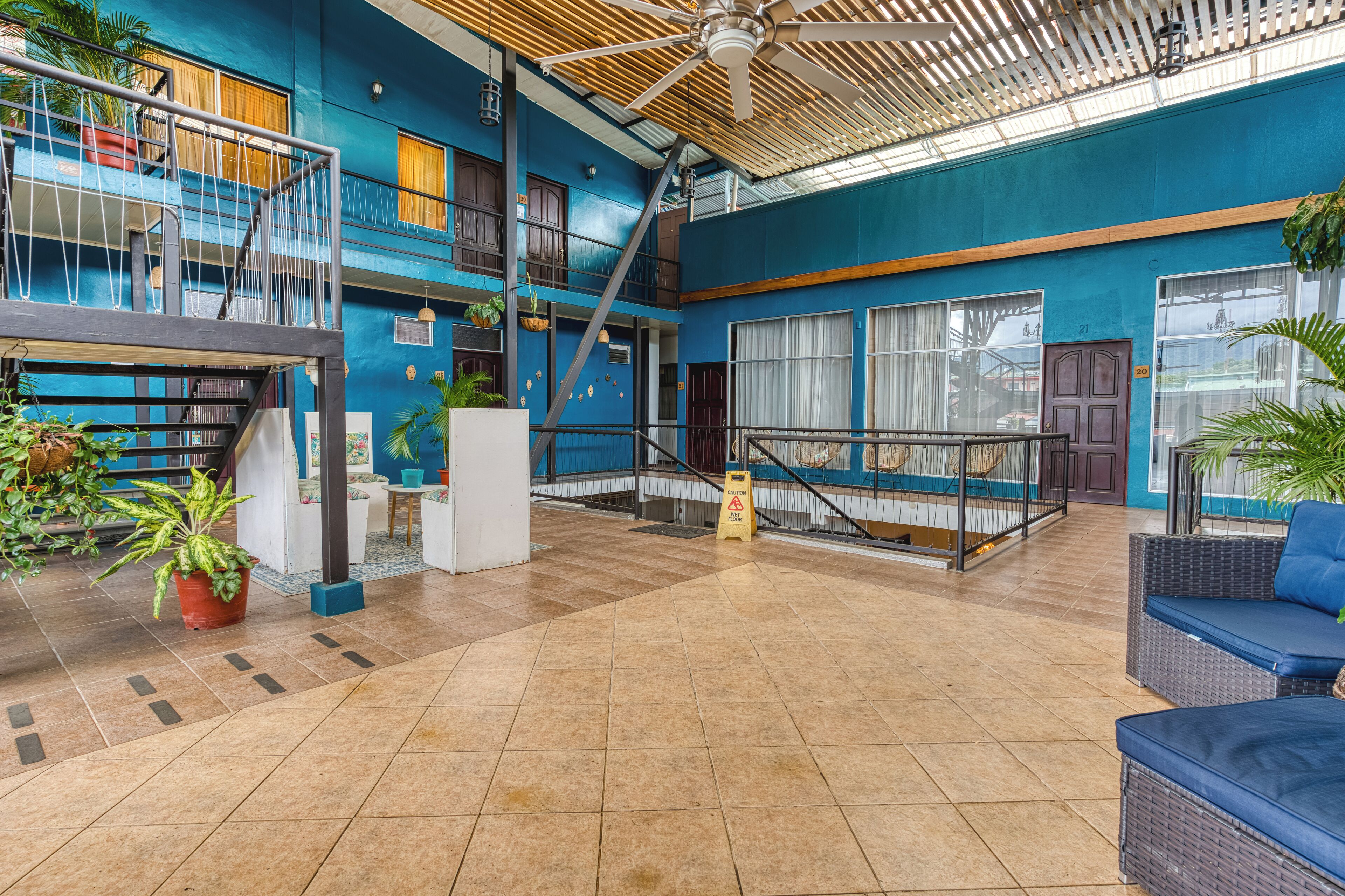 A spacious indoor area with a high ceiling, tiled flooring, and a variety of seating options including a blue sofa and wicker chairs.