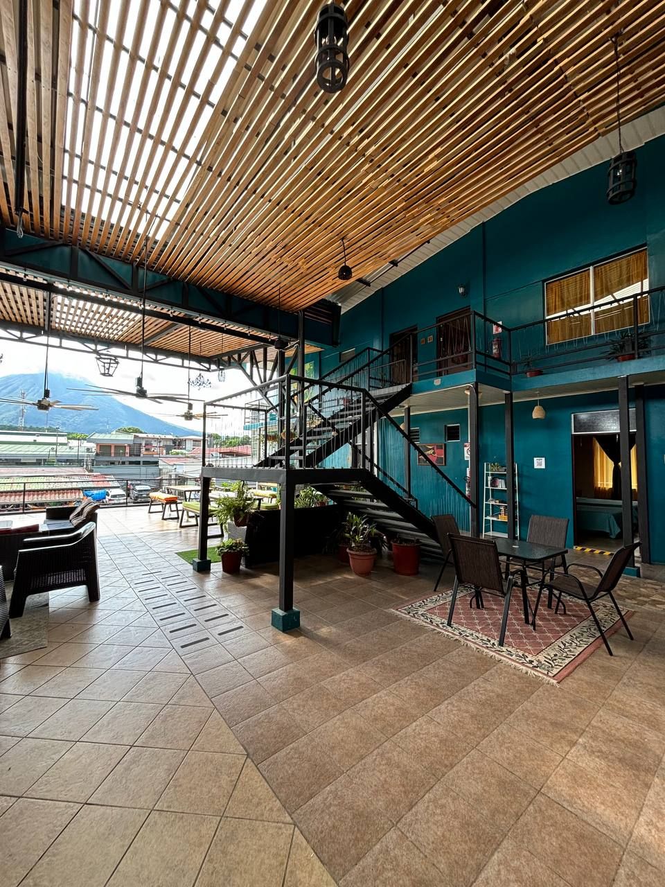A spacious indoor area with a wooden ceiling, a staircase, and a view of a mountain.