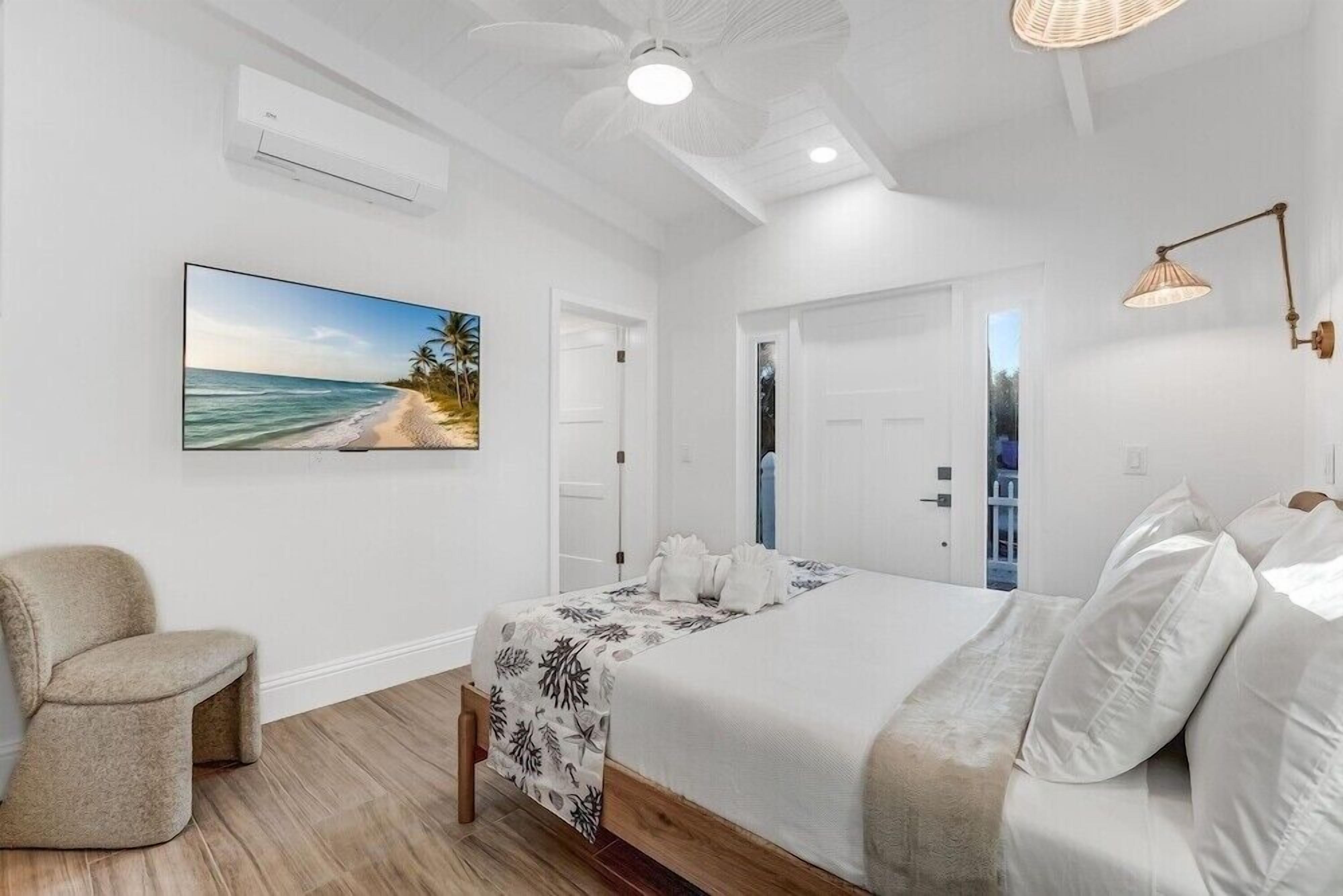 Une chambre à coucher avec un lit, une chaise, un tableau représentant une plage et un ventilateur de plafond.