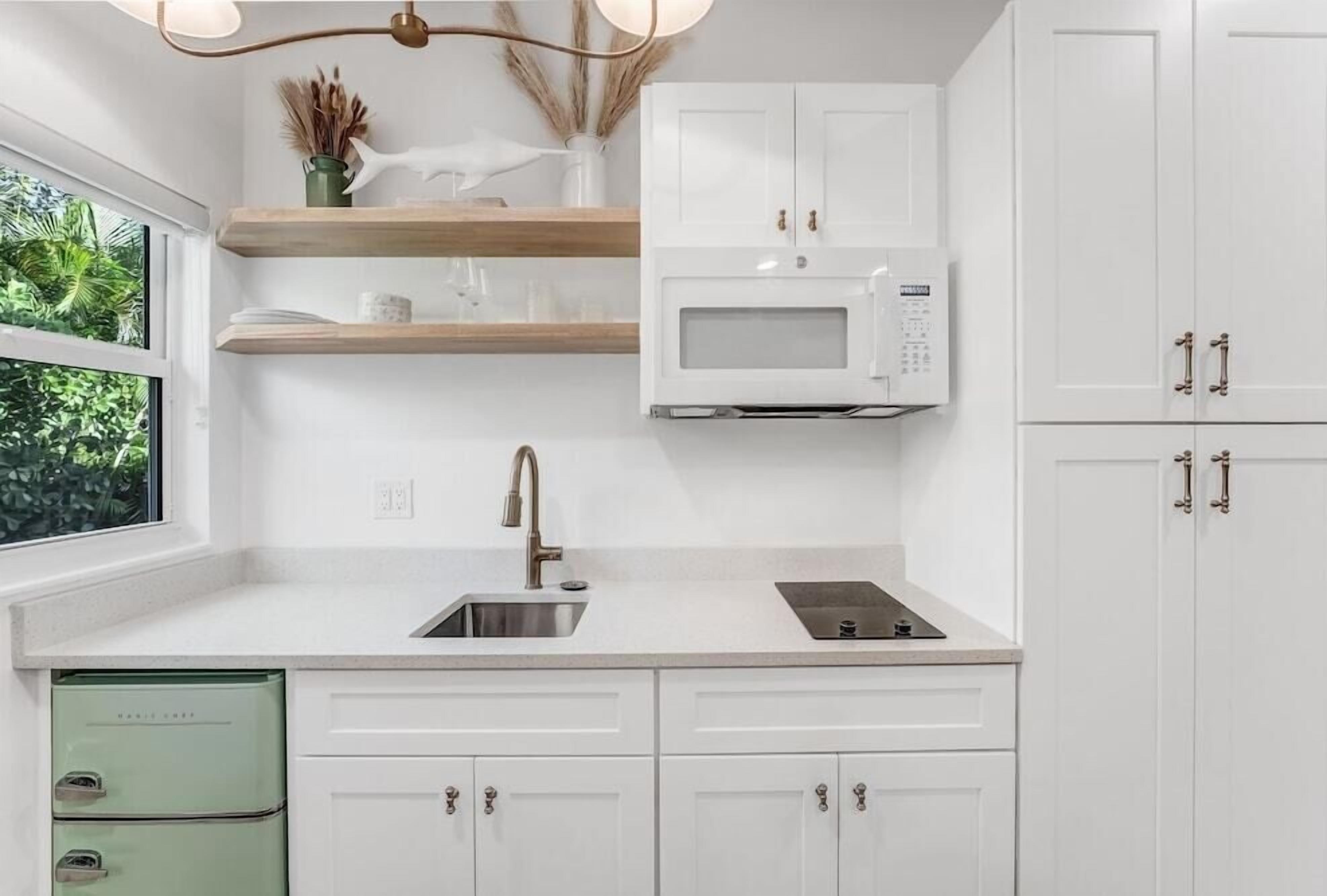 A modern kitchen with white cabinets, a built-in microwave, and a window with a view of greenery.