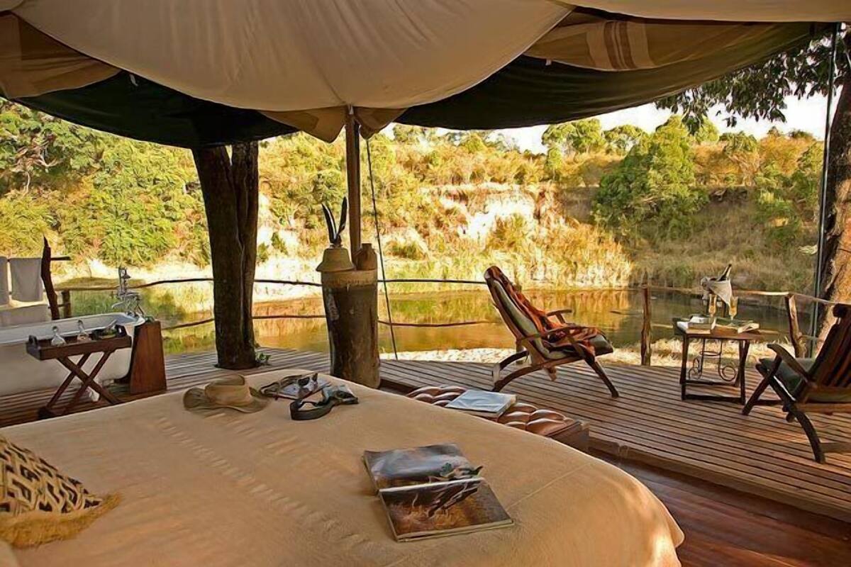 Una cama con vistas a un paisaje natural, una terraza de madera y una mesa con una silla.