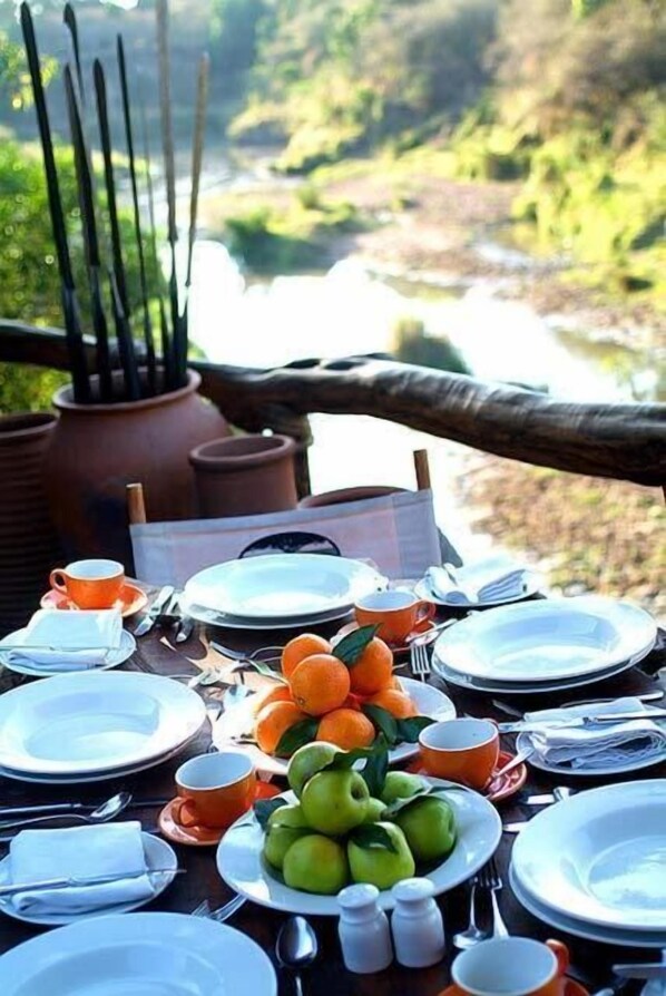 A table set outdoors with plates, cups, and utensils, surrounded by a natural landscape.