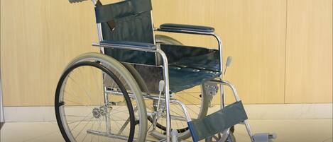 Un fauteuil roulant doté d’une structure métallique et de grandes roues, placé dans une pièce dont le sol est carrelé et dont le mur, sobre, sert de fond.