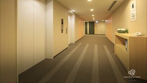 A hotel corridor with carpeted floors, a reception desk, and an elevator. - Daiwa Roynet Hotel YOKOHAMA-KANNAI (Yokohama)