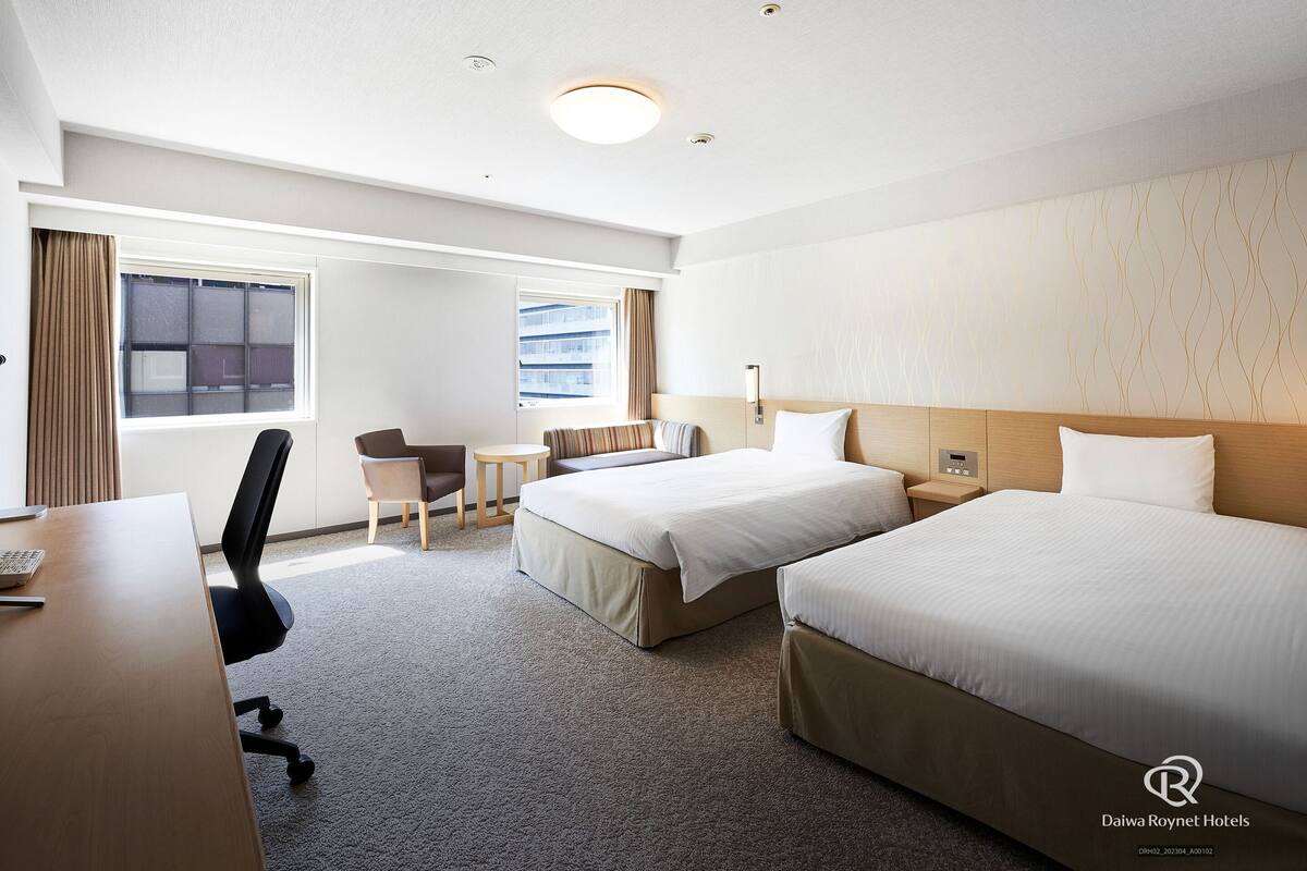A hotel room with two beds, a desk, a chair, and a small table.