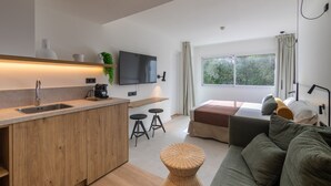 A modern kitchen with a built-in sink, bar stools, a flat-screen TV, and a large window with curtains.