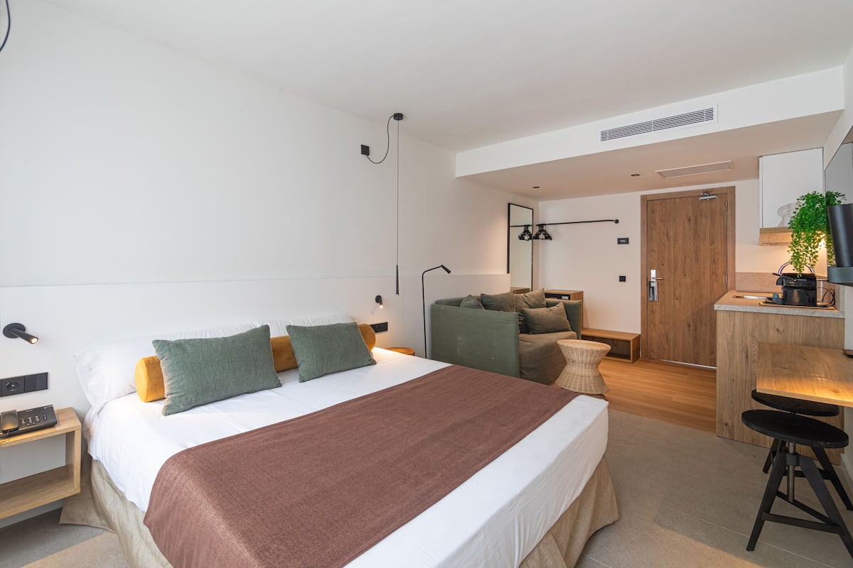A modern bedroom with a large bed, a desk, and a small seating area.